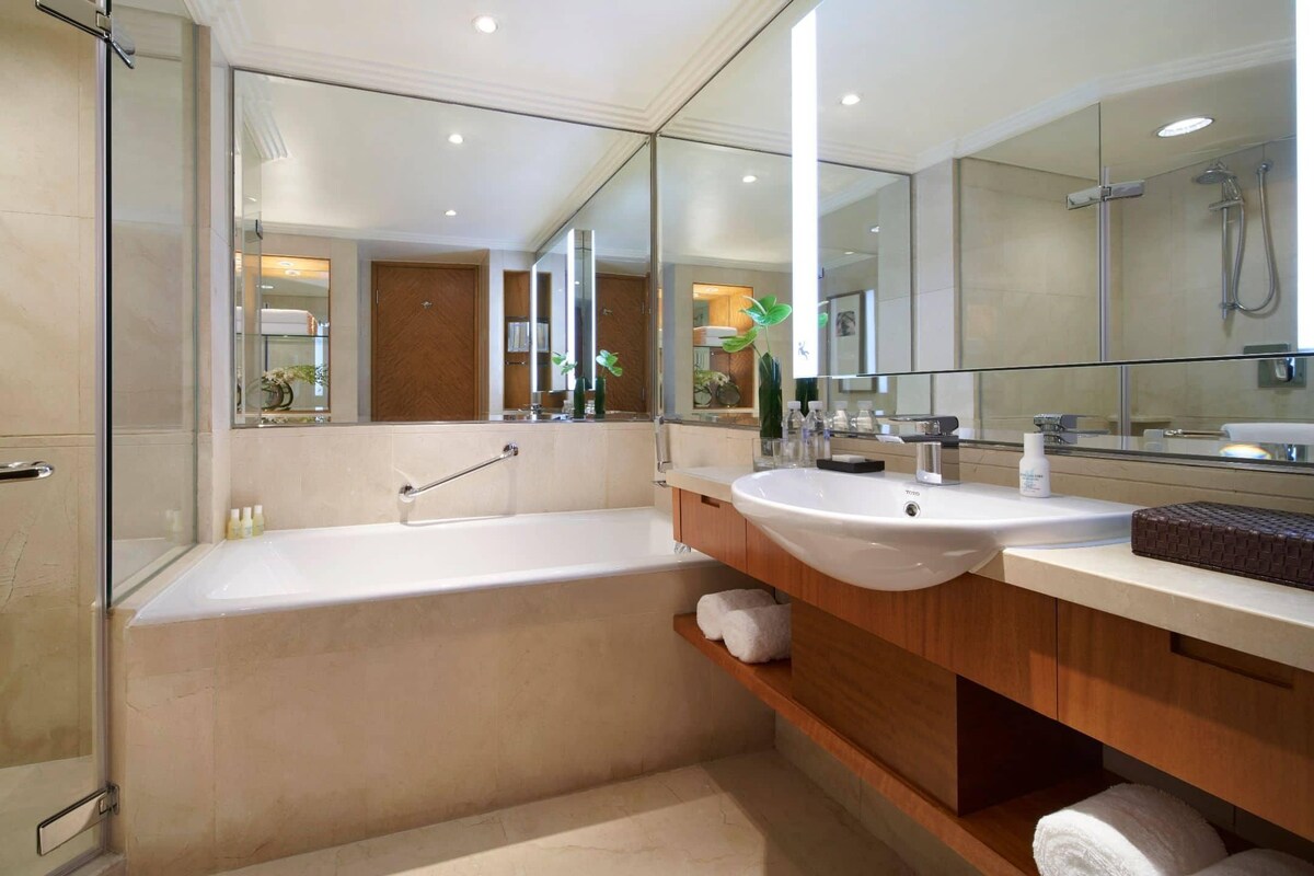 A modern bathroom with a bathtub, two sinks, a glass shower enclosure, and a large mirror.