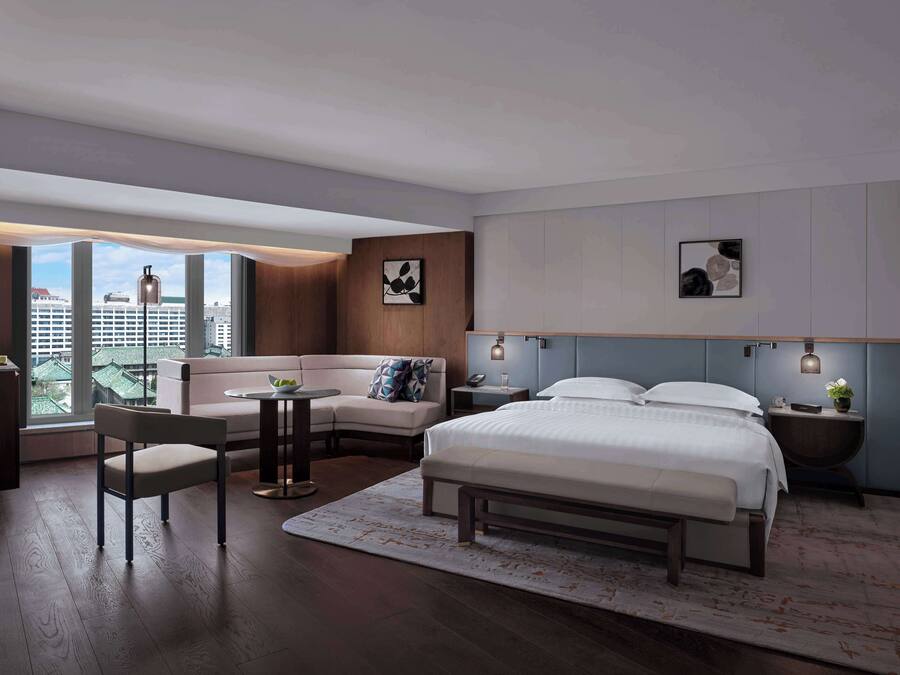 Een moderne hotelkamer met een groot bed, een bank, een bureau en uitzicht op de stad.