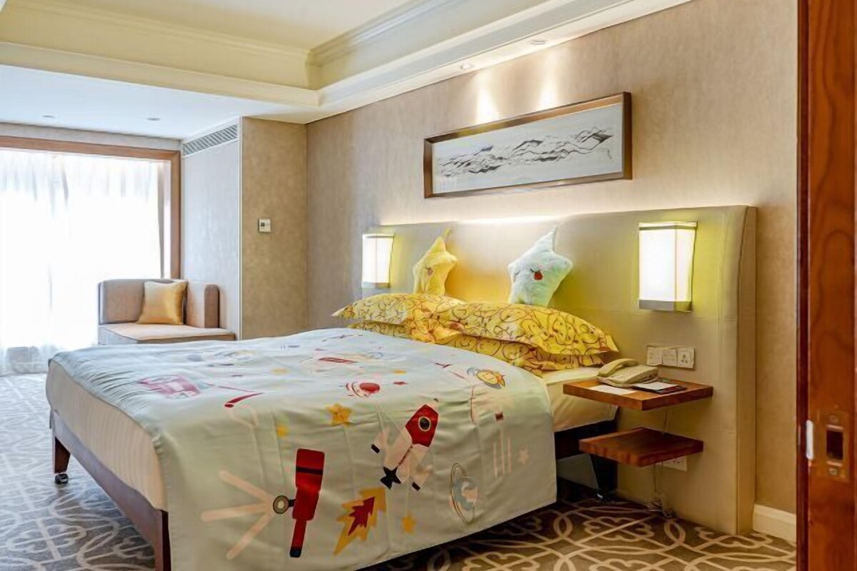 A hotel room with a bed, bedside table, lamp, and a painting on the wall.