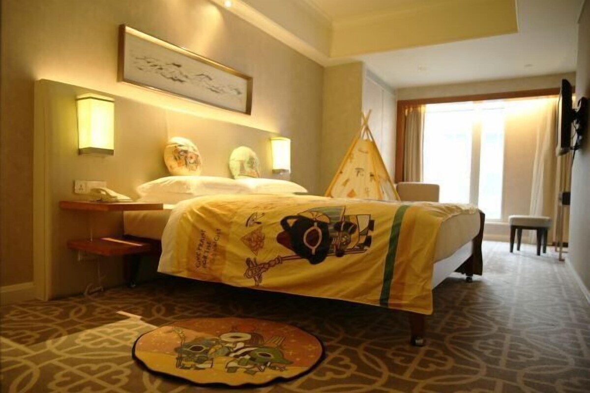 A hotel room with a bed, bedside table, lamp, and a painting on the wall.