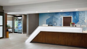 Un espace d’accueil au design moderne, comprenant un comptoir de réception, un mur agrémenté de textes et de motifs graphiques, et un réfrigérateur contenant des boissons.