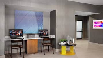 Un área de recepción moderna con dos monitores, un escritorio, sillas, una pequeña mesa con base amarilla y una gran obra de arte abstracta en la pared.