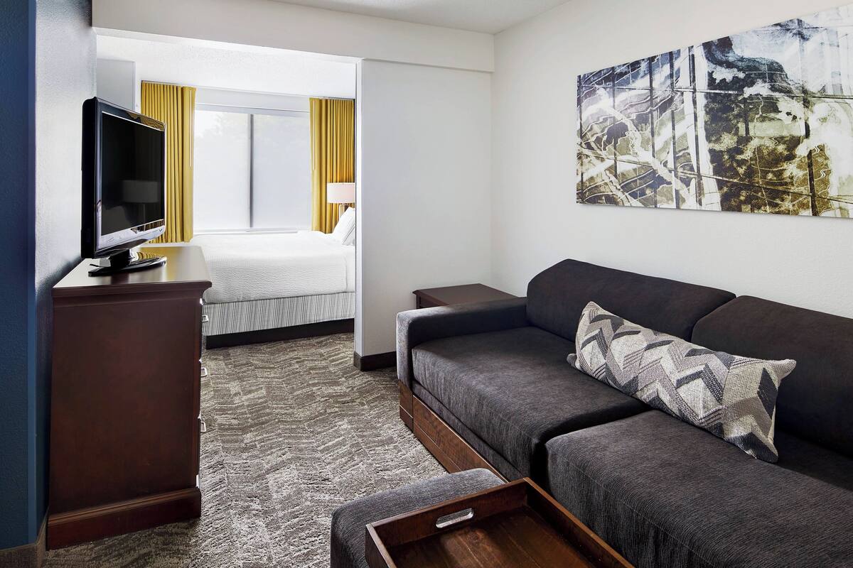 Een hotelkamer met een bed, een bank, een televisie en een schilderij aan de muur.