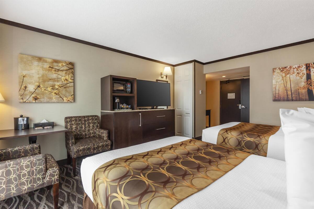 A hotel room with a bed, two armchairs, a desk with a television, and artwork on the walls.