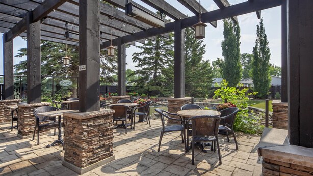 En udendørs terrasse med stensøjler, fletmøbler og en pergola.