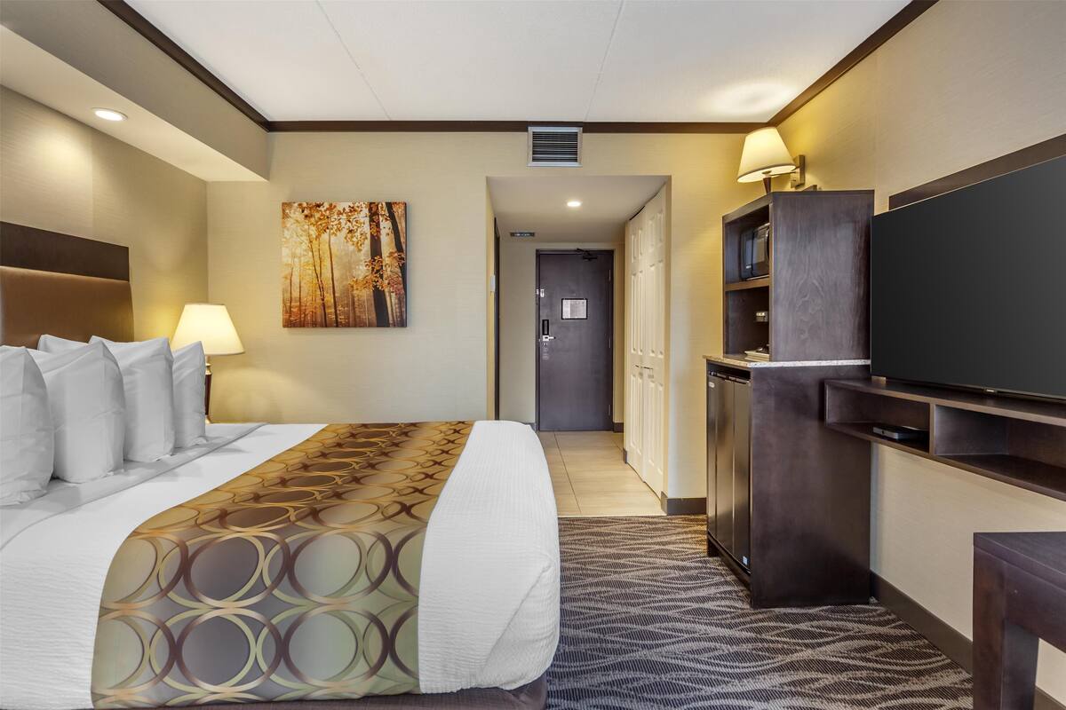A hotel room with a large bed, a flat-screen TV, a desk, and a painting on the wall.