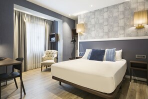 Moderni hotellihuone, jossa on suuri sänky, työpöytä, tuoli ja televisio.