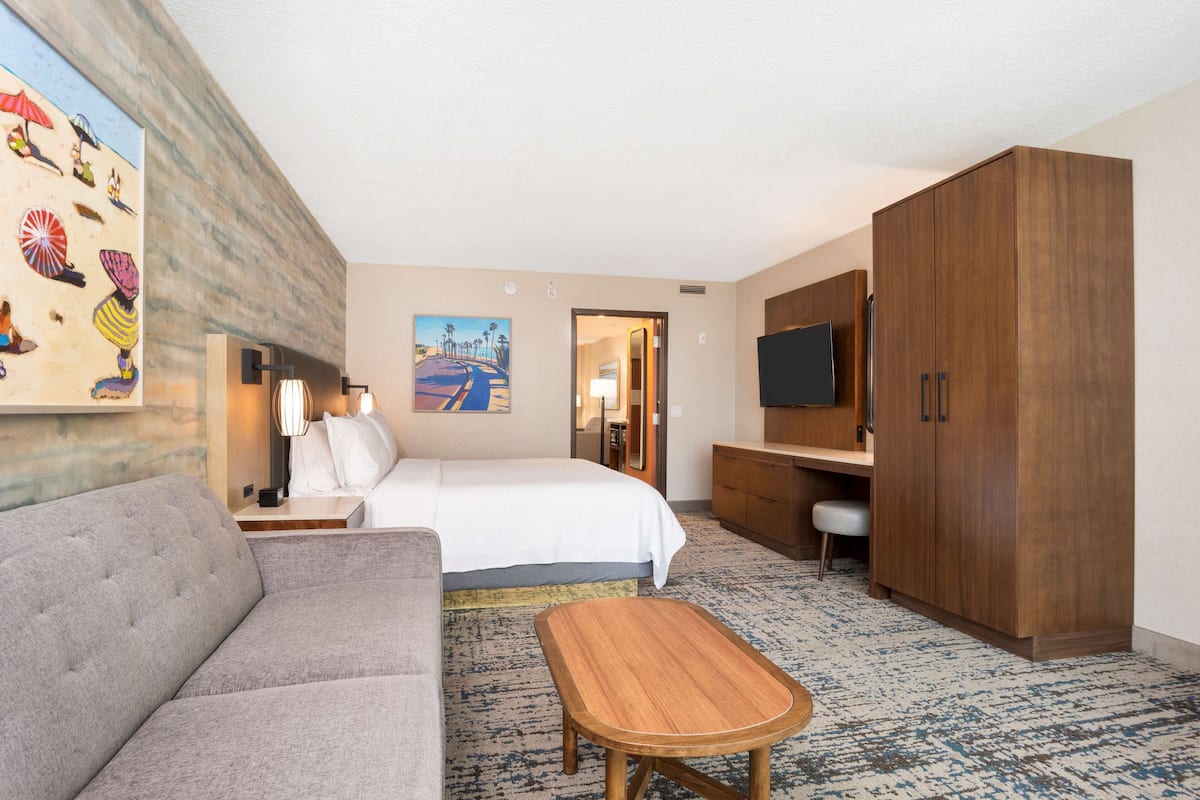 A hotel room with a bed, a sofa, a wooden table, a TV, and a wardrobe.
