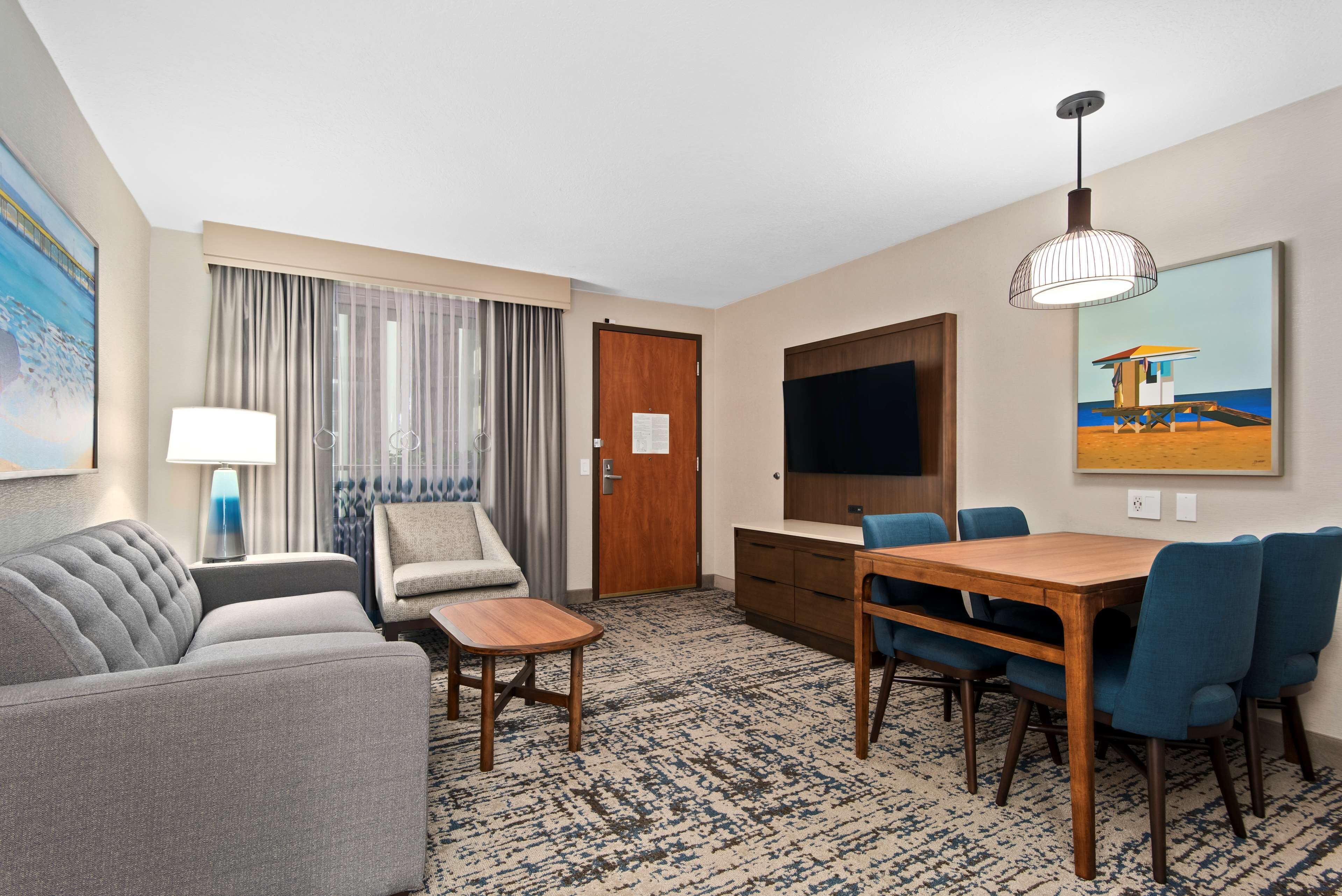 A hotel room with a sofa, a small table, a TV, a dining table with chairs, and a painting on the wall.