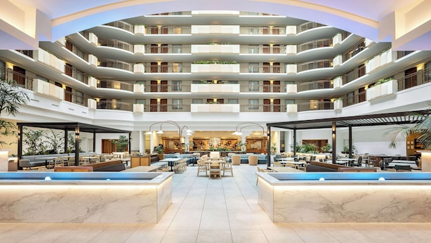 Un hall d’hôtel à plusieurs niveaux, doté d’une piscine centrale, d’espaces de détente et d’une architecture moderne.