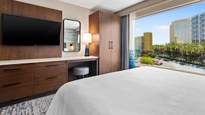 Une chambre d’hôtel dotée d’un grand lit, d’un téléviseur à écran plat fixé au mur, d’un bureau avec une lampe et offrant une vue sur le paysage urbain grâce à de grandes fenêtres.
