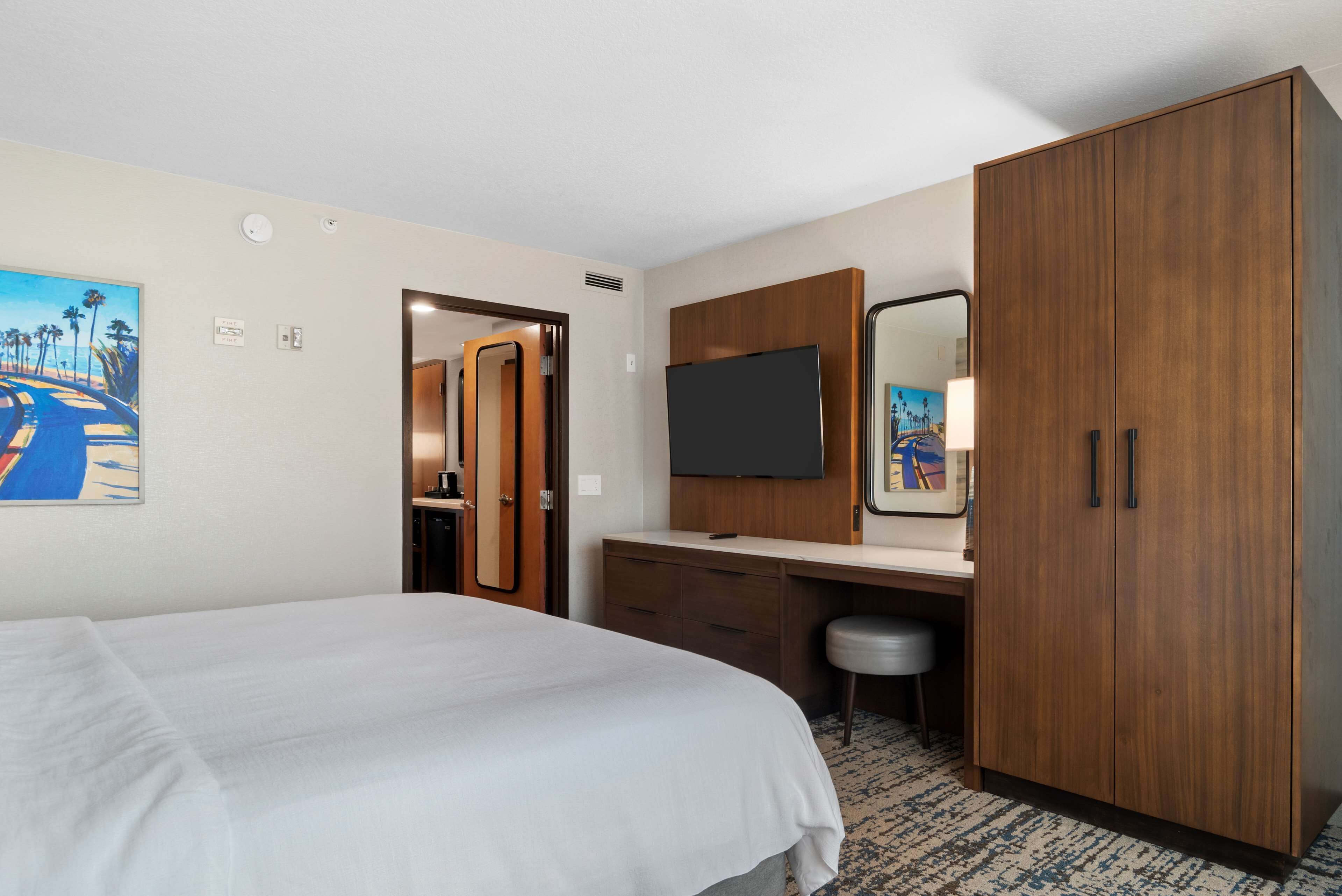 Une chambre d’hôtel comprenant un lit, un bureau avec un miroir, une armoire et un téléviseur.