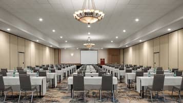 Un salón de conferencias con filas de mesas, sillas y una pantalla grande al frente.