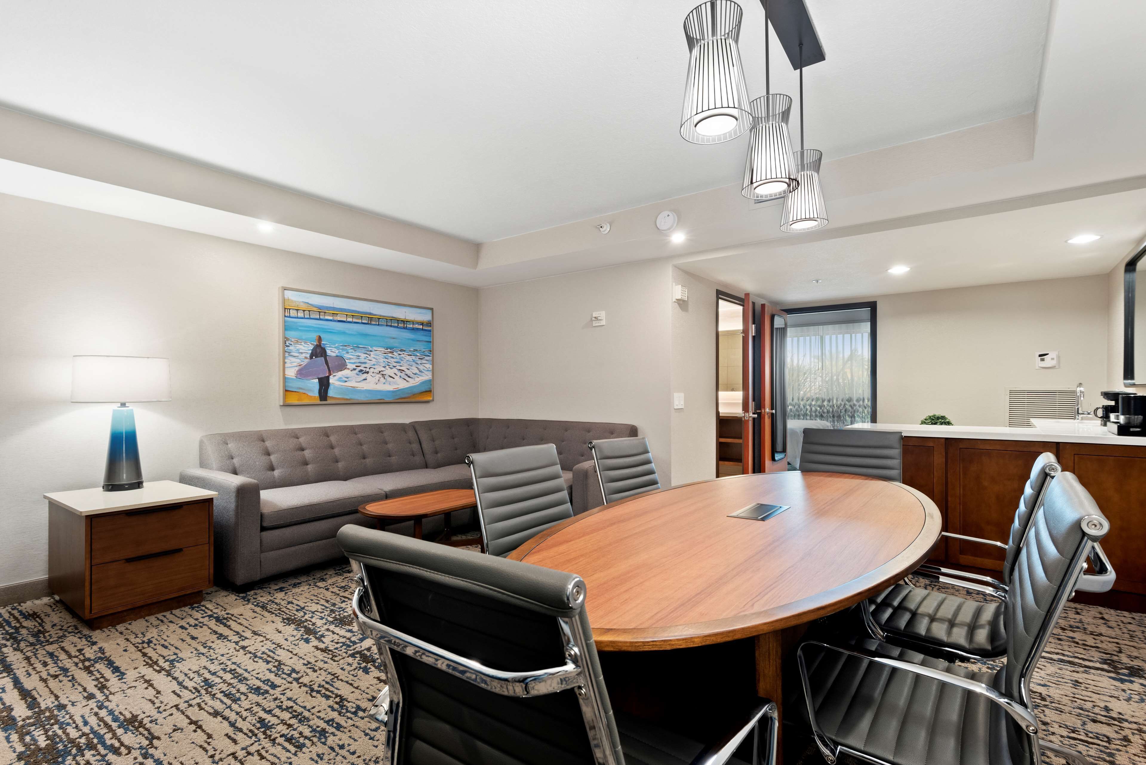 A conference room with a round table, leather chairs, a sofa, and a painting of a beach scene.