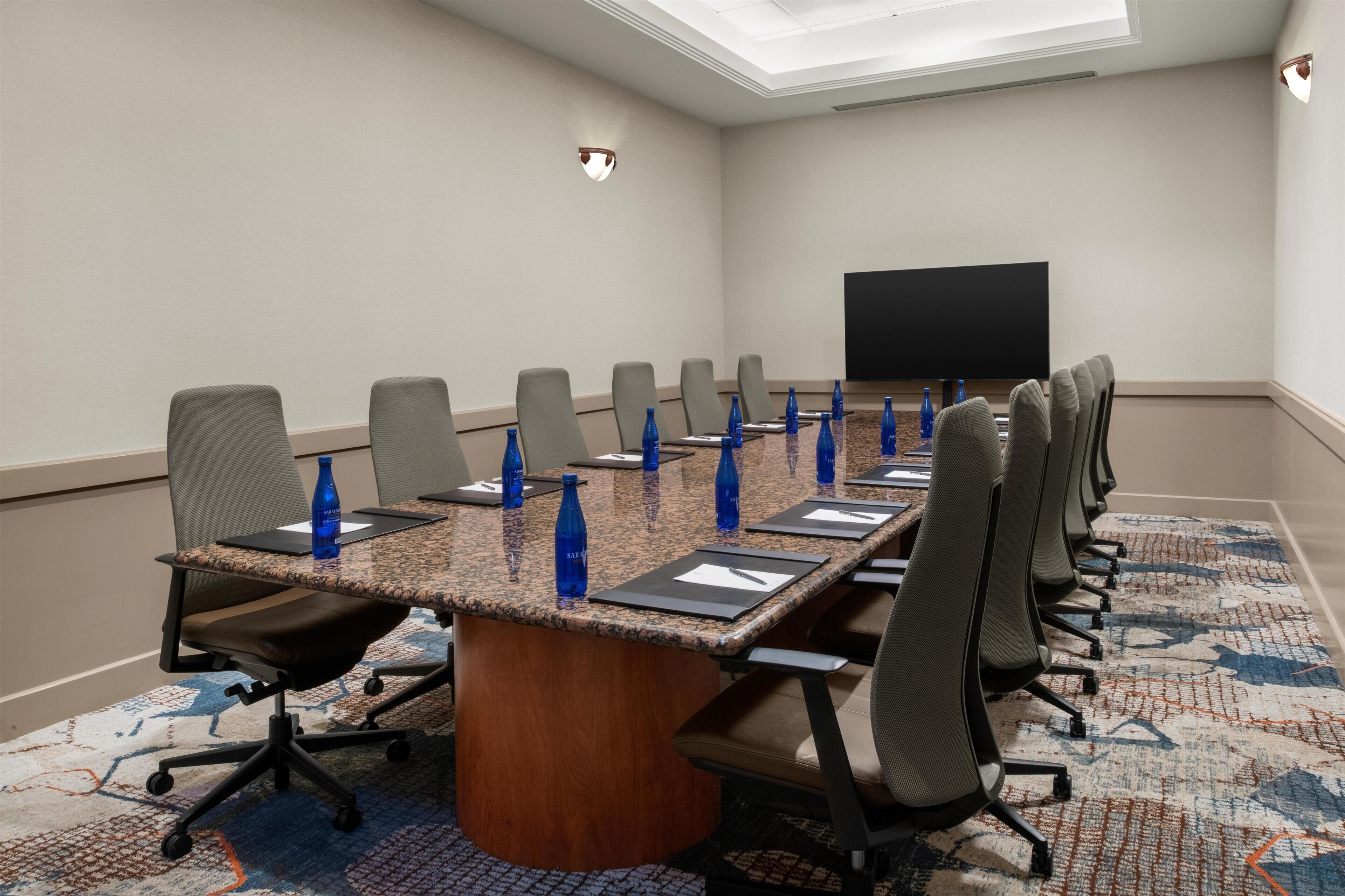 A conference room with a long table, chairs, a flat-screen TV, and water bottles.