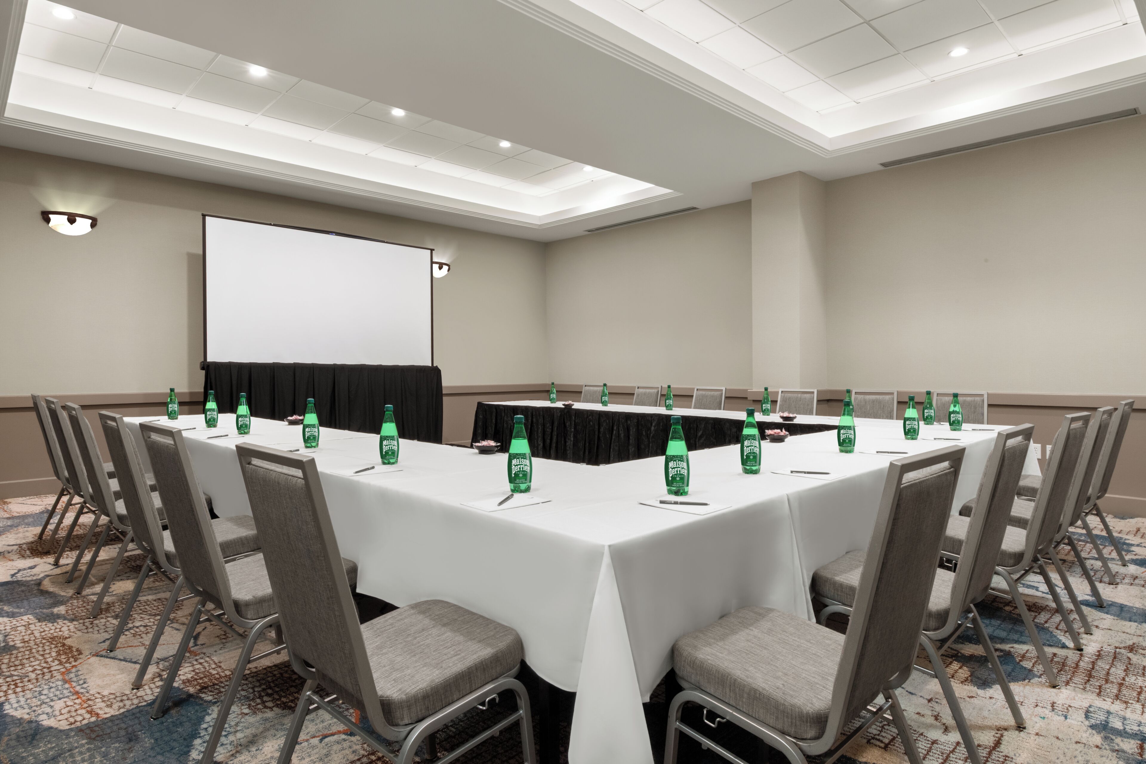 A conference room with a long table, chairs, a projector screen, and water bottles.