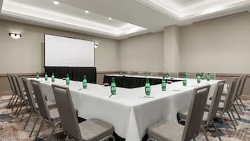 A conference room with a long table, chairs, a projector screen, and water bottles.
