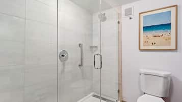 Ein modernes Badezimmer mit einer gläsernen Dusche, einer weißen Toilette und einem Strandbild an der Wand.
