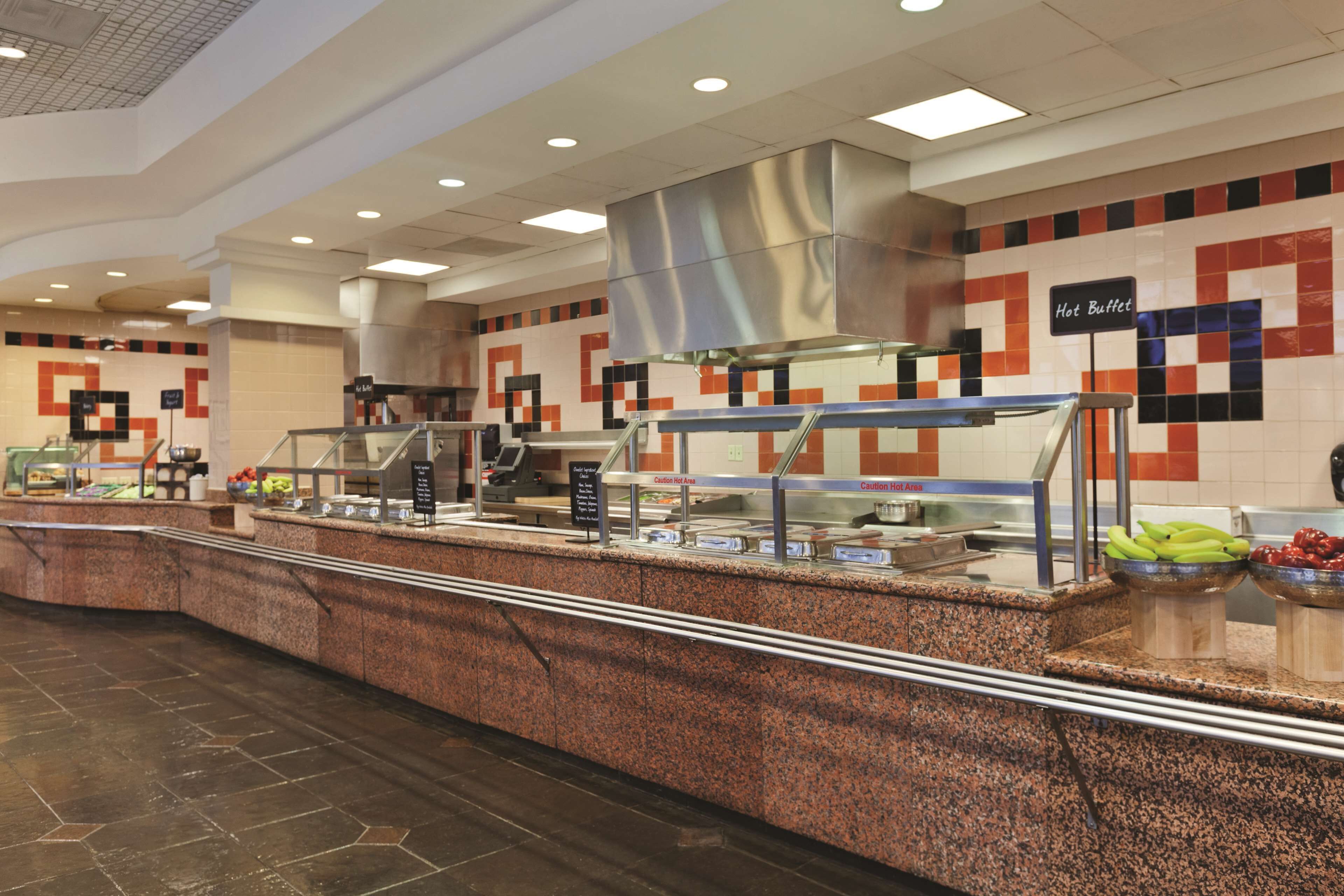 A buffet area with a stainless steel counter, a sign indicating 'Hot Buffet', and a tiled wall with a geometric pattern.
