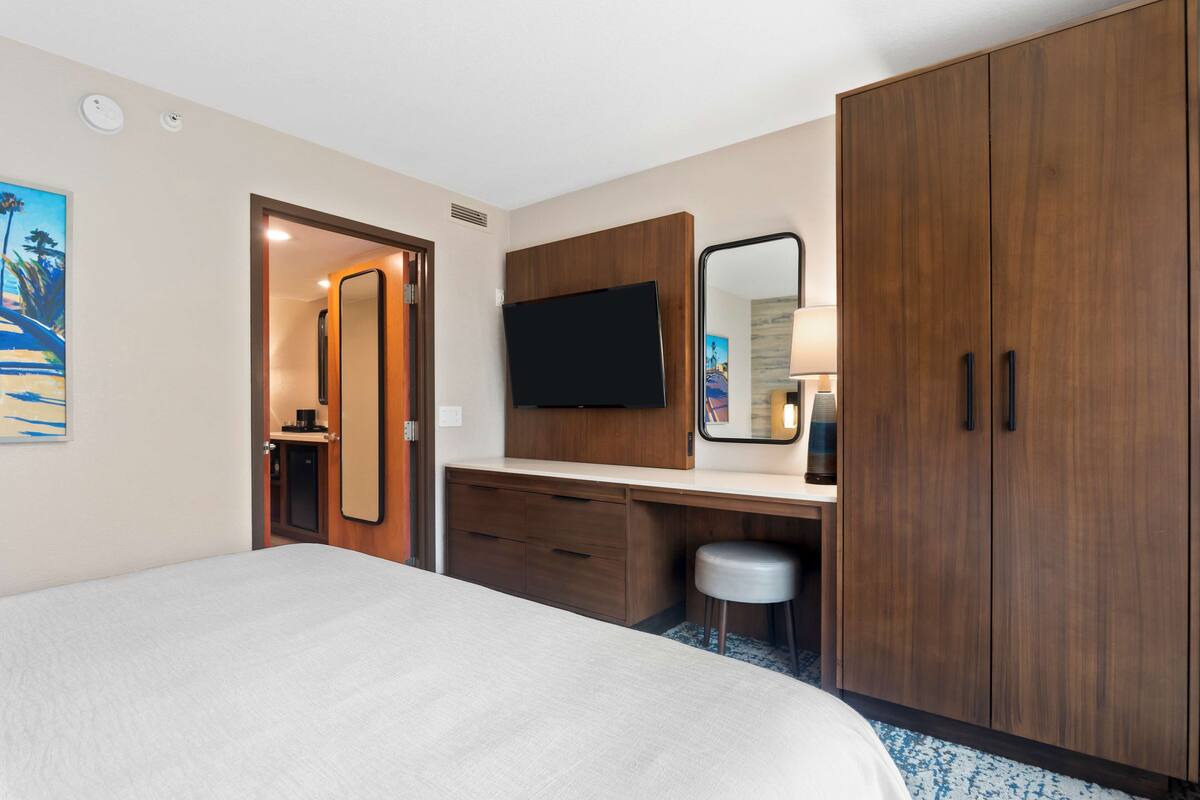 A hotel room with a bed, a desk with a mirror, a television, and a wardrobe.