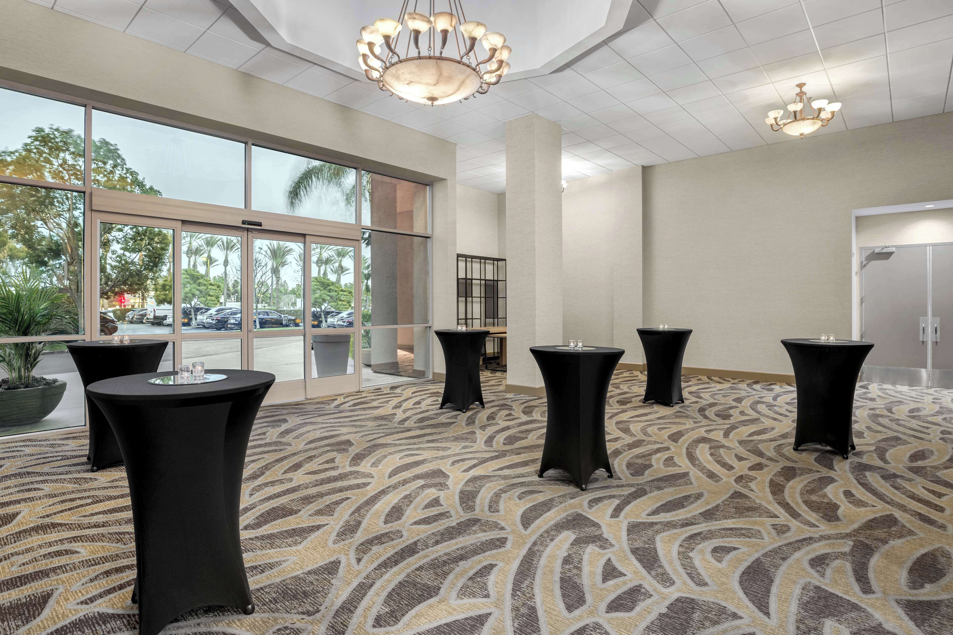 A spacious room with a patterned carpet, large windows, and black tables with glasses.