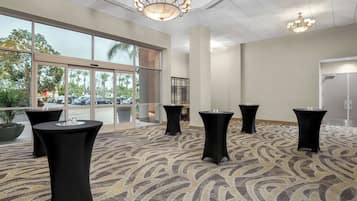 A spacious room with a patterned carpet, large windows, and black tables with glasses.