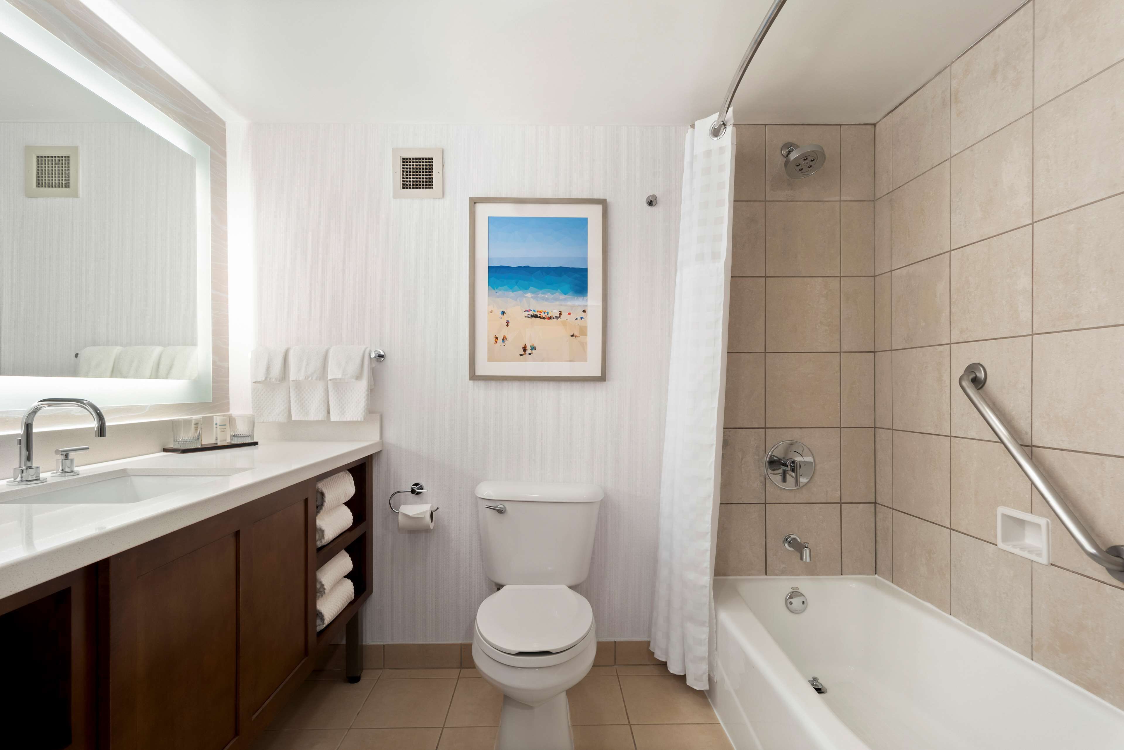A bathroom with a bathtub, toilet, sink, and a framed beach picture on the wall.