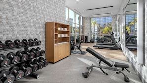 Une salle de sport moderne équipée de supports pour les poids, d’appareils de cardio et de grandes fenêtres offrant une vue sur l’extérieur.