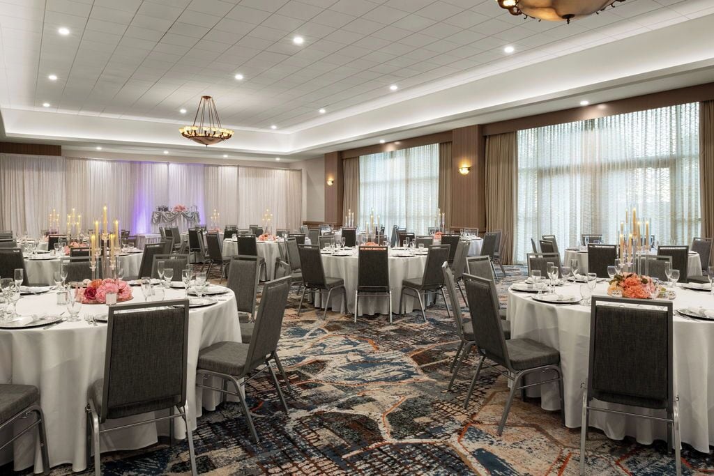 Een feestzaal met ronde tafels, stoelen en een vloerkleed.