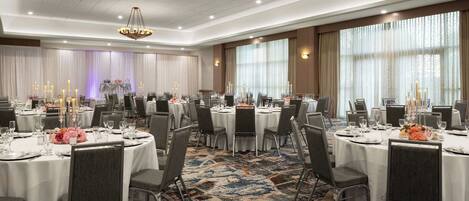 A banquet hall with round tables, chairs, and a carpeted floor.