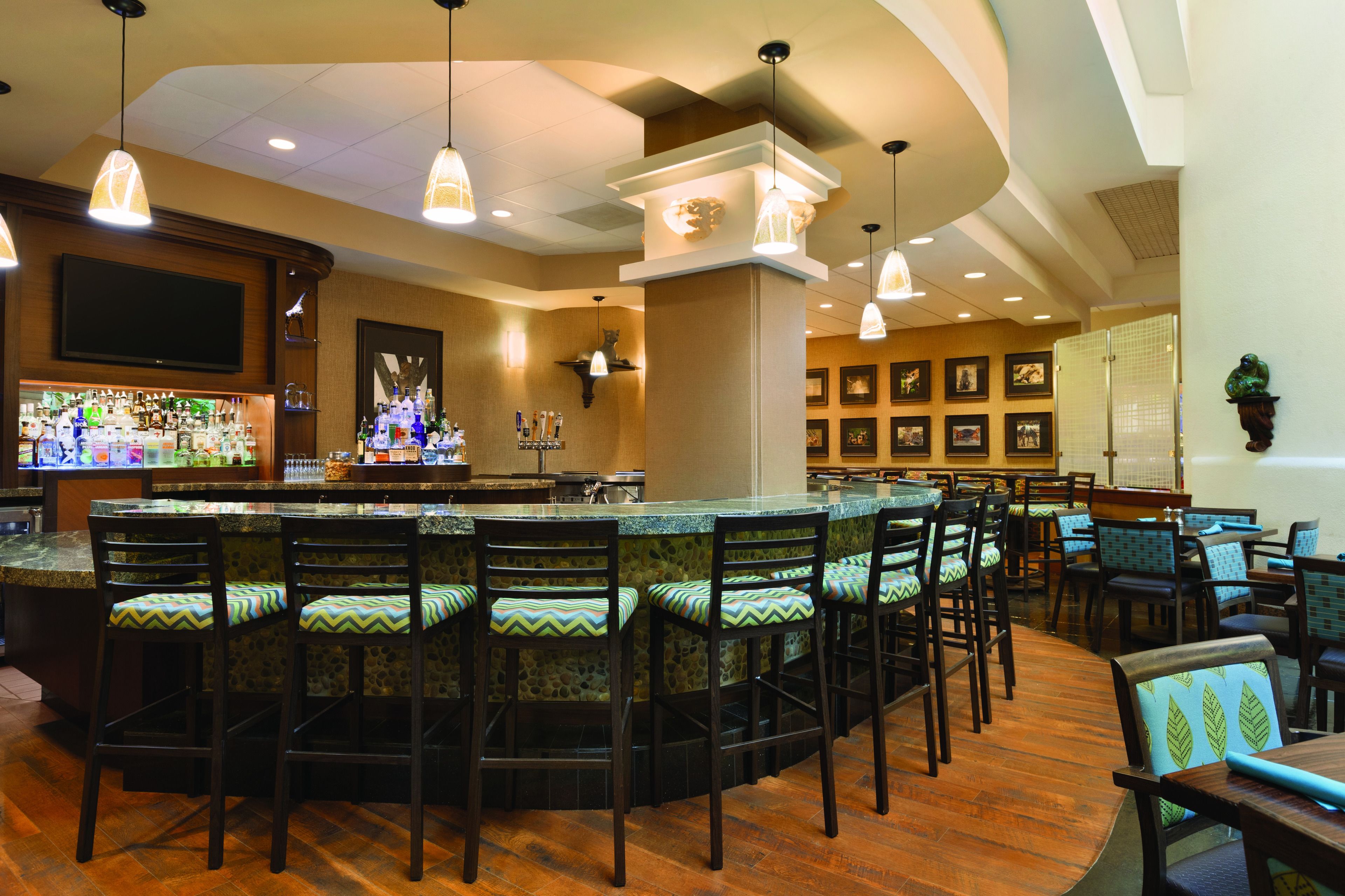 A bar area with a long counter, multiple bar stools, and a television screen.
