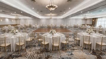 A large banquet hall with round tables, gold chairs, and white tablecloths.