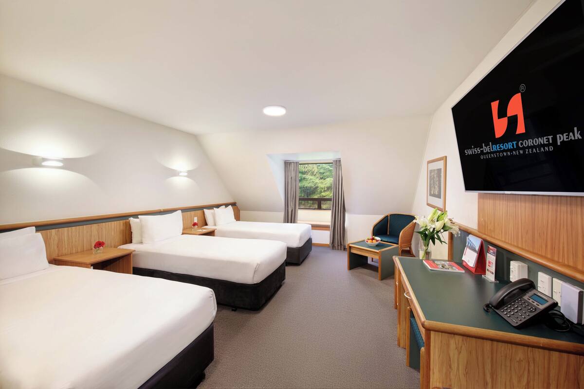 Ein Hotelzimmer mit zwei Betten, einem Schreibtisch mit Telefon und einem an der Wand befestigten Fernseher.