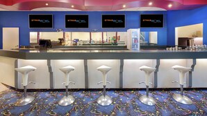 Un espace bar aux couleurs bleu et rose, avec plusieurs téléviseurs diffusant des images du « Strike Bowl » et des tabourets de bar.