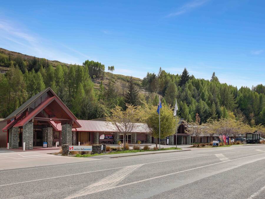 A hotel with a red roof and stone facade, situated in a mountainous area with a clear sky.