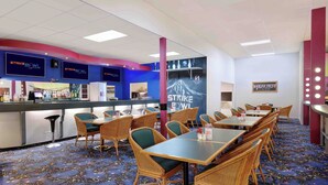 Un restaurant aux couleurs bleu et blanc, avec un comptoir doté d’un écran numérique, des chaises en osier et un sol recouvert de moquette.