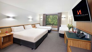 Une chambre d’hôtel avec un grand lit, deux tables de chevet, un bureau avec un téléphone et un écran de télévision affichant le nom de l’hôtel.