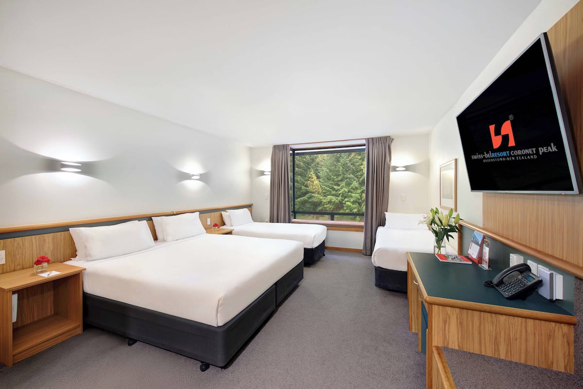 Ein Hotelzimmer mit einem großen Bett, zwei Nachttischen, einem Schreibtisch mit Telefon und einem Fernseher, der den Namen des Hotels anzeigt.