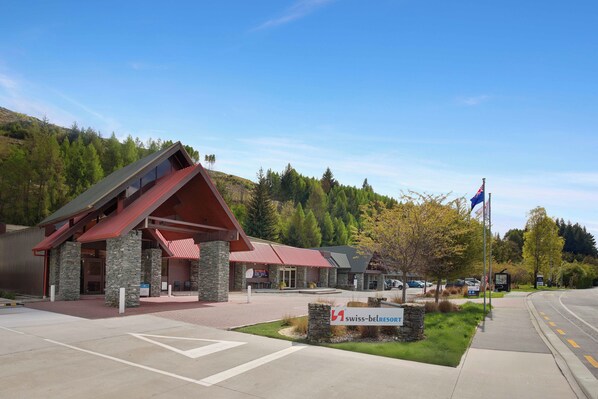 A hotel with a red roof and stone facade, surrounded by trees and a clear sky. - Swiss-Belresort Coronet Peak (Arthur's Point)