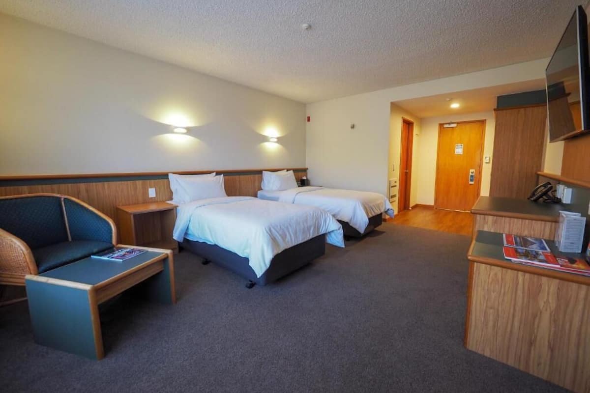 Ein Hotelzimmer mit zwei Betten, einem Schreibtisch, einem Sessel und einem Fernseher.
