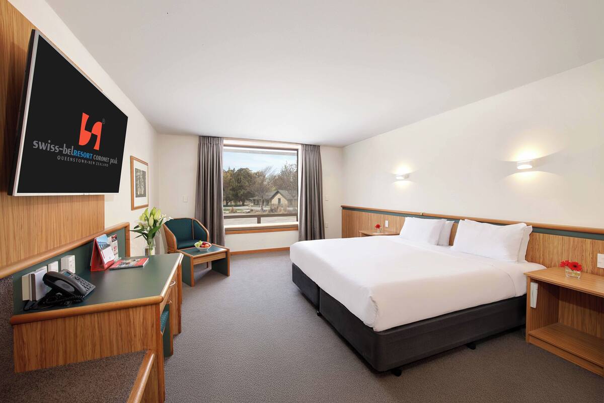 Ein Hotelzimmer mit Bett, Schreibtisch, Stuhl und einem großen Fenster.