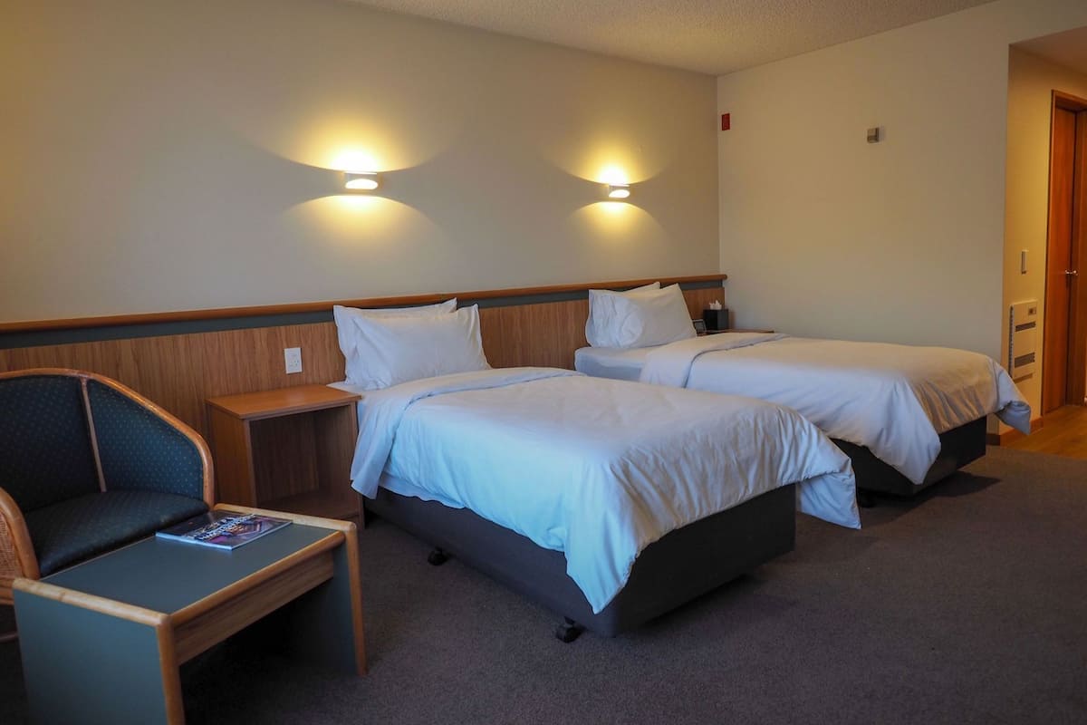 Ein Hotelzimmer mit zwei Betten, einem kleinen Tisch, einem Stuhl und zwei Wandleuchten.
