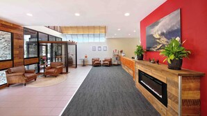 Un espace d’accueil moderne avec une cheminée, des fauteuils en cuir et un mur d’accent rouge.