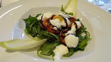 Un plato de comida con ensalada, tomates y salsa cremosa.