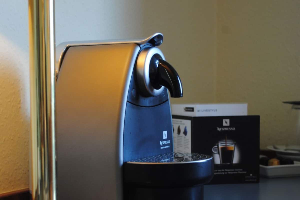 A coffee machine with a black base and a silver top, a lamp with a gold base, and a box labeled 'LIVESTYLE' in the background.