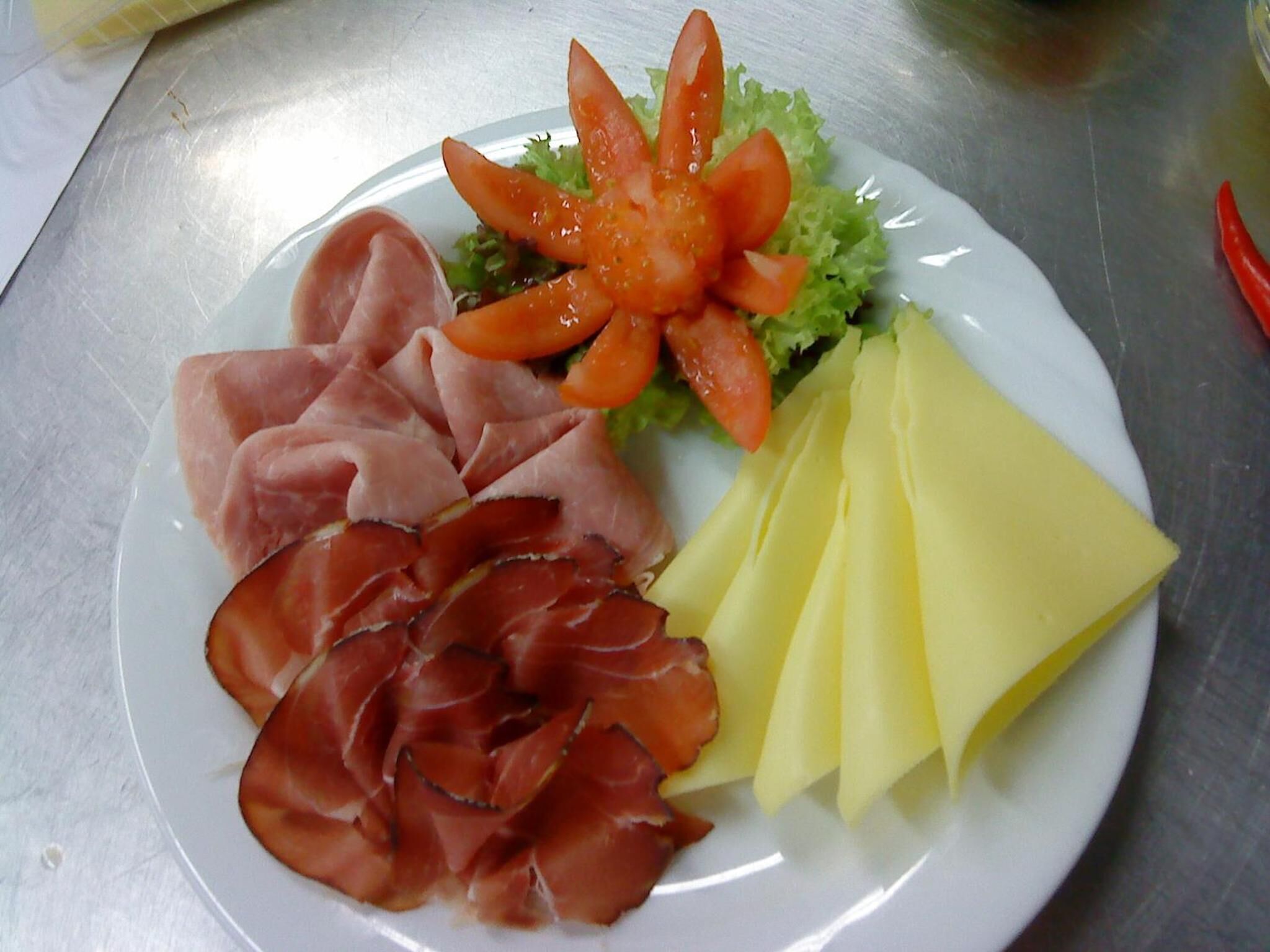 Een bord met plakjes ham, kaas en een tomaat.