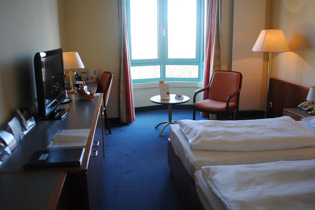 A hotel room with a bed, desk, chair, TV, lamp, and a window with curtains.