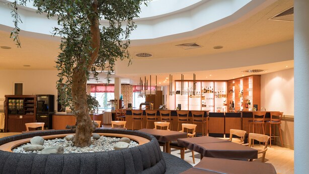 A modern hotel lobby with a central seating area, a bar, and a kitchen in the background. - Hotel am Rosengarten (Bad Wimpfen)