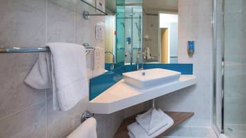 Un bagno moderno con box doccia in vetro, un lavandino bianco e uno scaffale in legno.