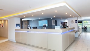 A hotel reception area with a modern design, featuring a reception desk, digital check-in kiosks, and a visible clock. - Holiday Inn Express Milton Keynes by IHG (Milton Keynes)